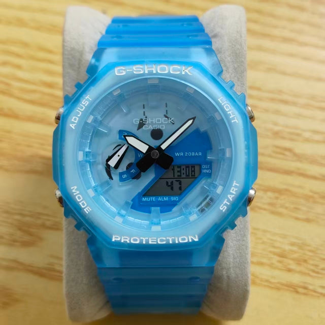 A blue G-Shock Casio watch with a translucent blue resin case and strap, displayed on a gray stand over a light wood background.