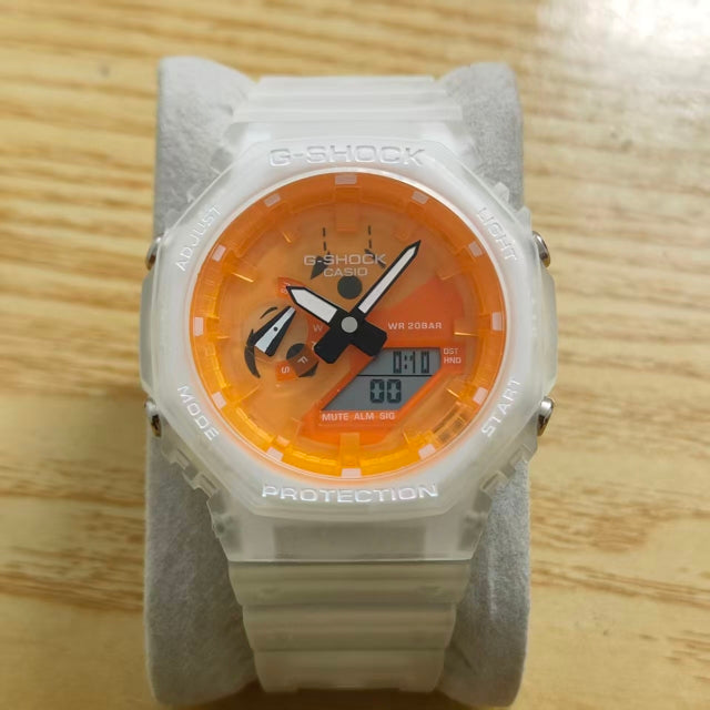 A Casio G-Shock analog watch with a translucent white resin case and strap, featuring a vibrant orange dial with black hands and a digital display, resting on a gray display stand over a light wood surface.