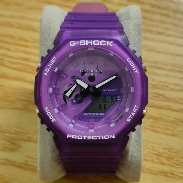 A purple G-Shock Casio watch with a matching translucent purple strap, displayed on a light gray stand over a wooden surface.