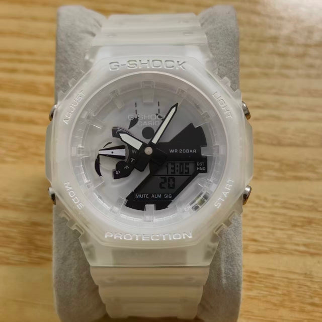 A G-Shock analog-digital watch with a translucent white resin case and strap, displayed on a gray velvet stand over a light wood surface.