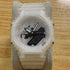 A G-Shock analog-digital watch with a translucent white resin case and strap, displayed on a gray velvet stand over a light wood surface.